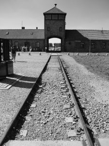 Durch ein hölzernes Tor führen Eisenbahngleise, auf denen Juden in Waggons in das Vernichtungslager transportiert wurden.